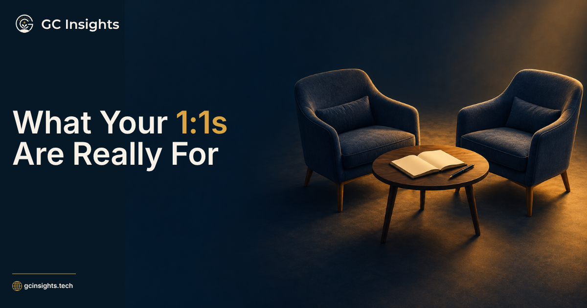 “What Your 1:1s Are Really For” beside two chairs and a small table with an open notebook, ready for a one-on-one conversation.